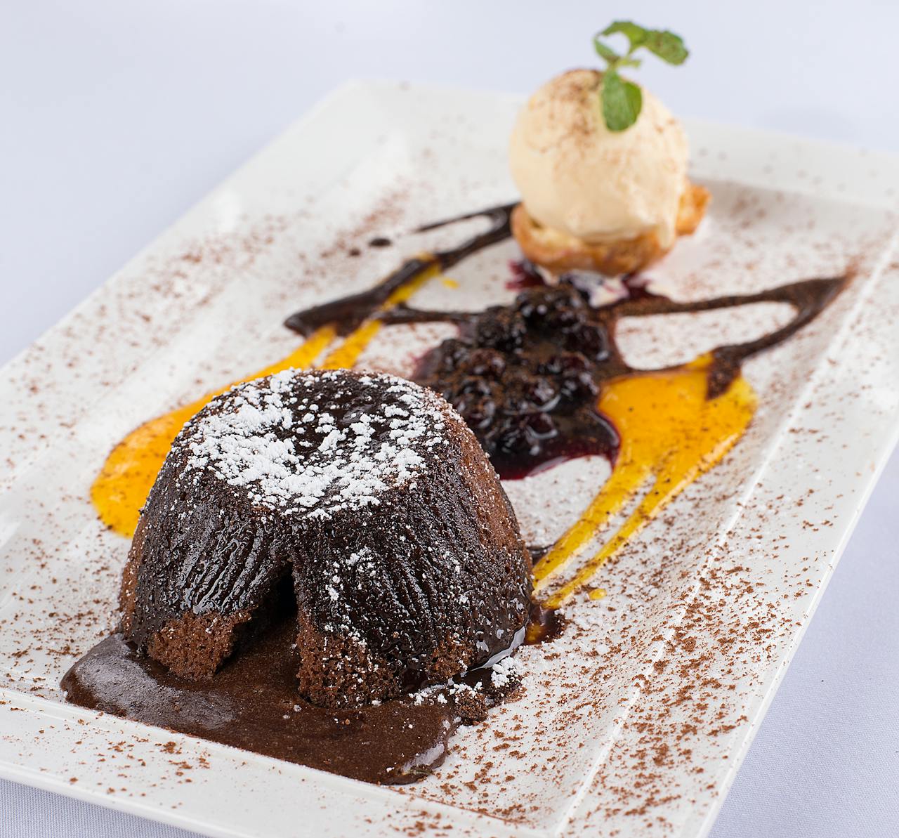 Mouthwatering chocolate lava cake served with ice cream and artistic sauce drizzle on a plate.